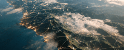 Aerial view of a coastline with illuminated cities and network lines connecting various points, symbolizing digital connectivity and communication.