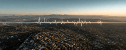 Aerial view of a suburban landscape with a digital soundwave graphic superimposed horizontally across the horizon at sunset.