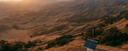 A small solar panel installation stands on a hillside, overlooking a vast expanse of rolling hills at sunset, helping to power equipment for the ShakeAlert seismic network in California.